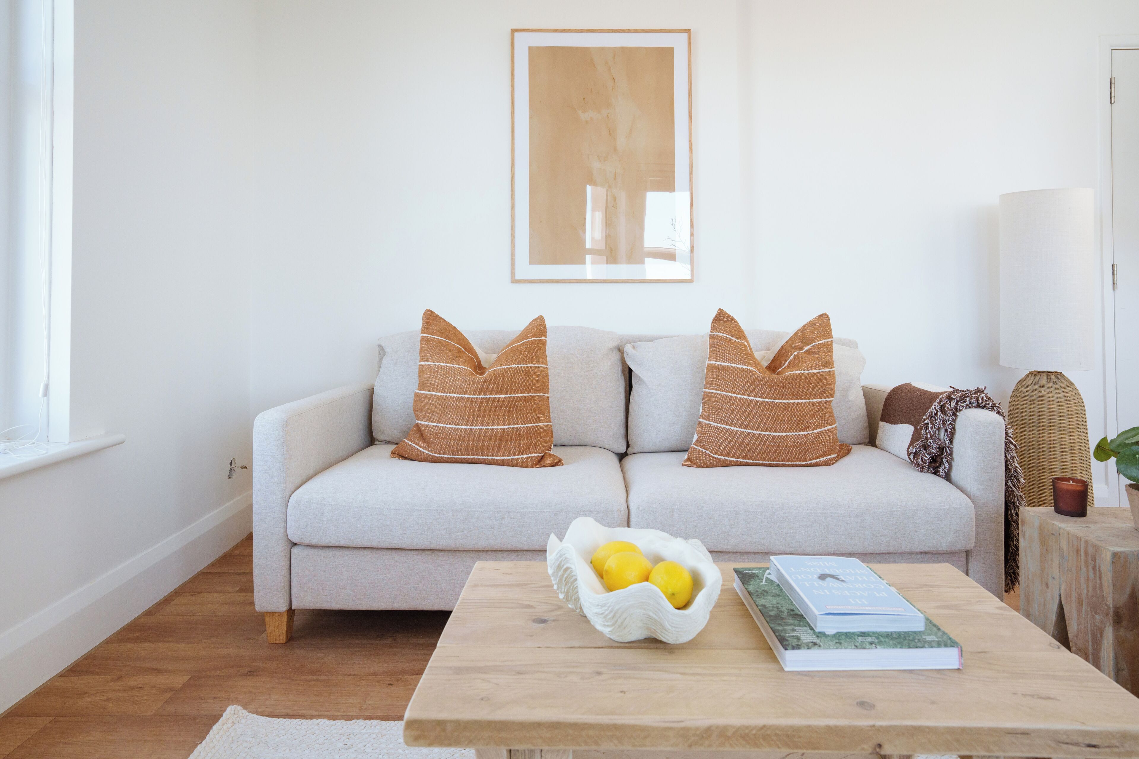 A living room with a sofa, cushions, a coffee table with a bowl of lemons, and a book.
