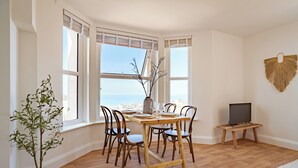 A dining area with a wooden table set for four, surrounded by chairs, a potted plant, and a television on a stand. - VESTO  Coastal Hideout (Newquay)
