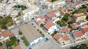 An aerial view of a residential area with houses, a central road, and a blue building with a sign. - Entire Algarve home for six (Armação de Pêra)