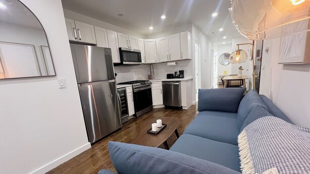 A modern kitchen with white cabinets, stainless steel appliances, and a wooden floor. - 4-bedroom apartment in the lower east side (New York)