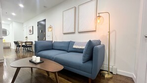 A modern living room with a blue sofa, a wooden coffee table, and a floor lamp. - 4-bedroom apartment in the lower east side (New York)