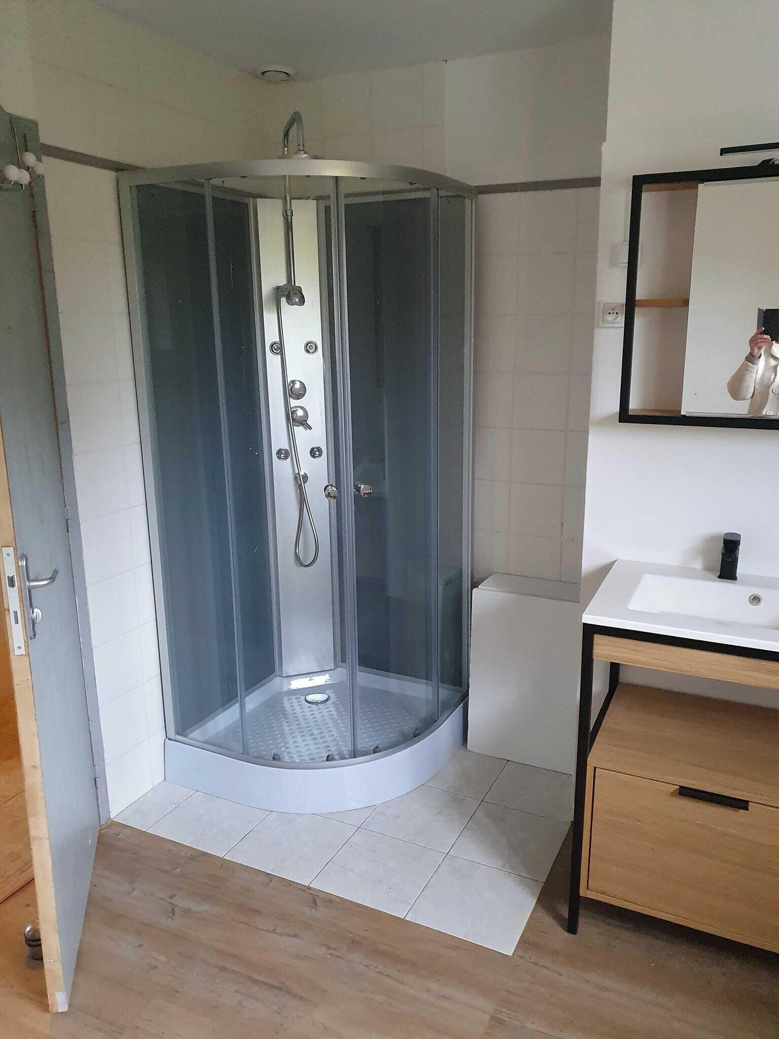 A corner shower enclosure with a glass door, a white sink, and a wooden cabinet.