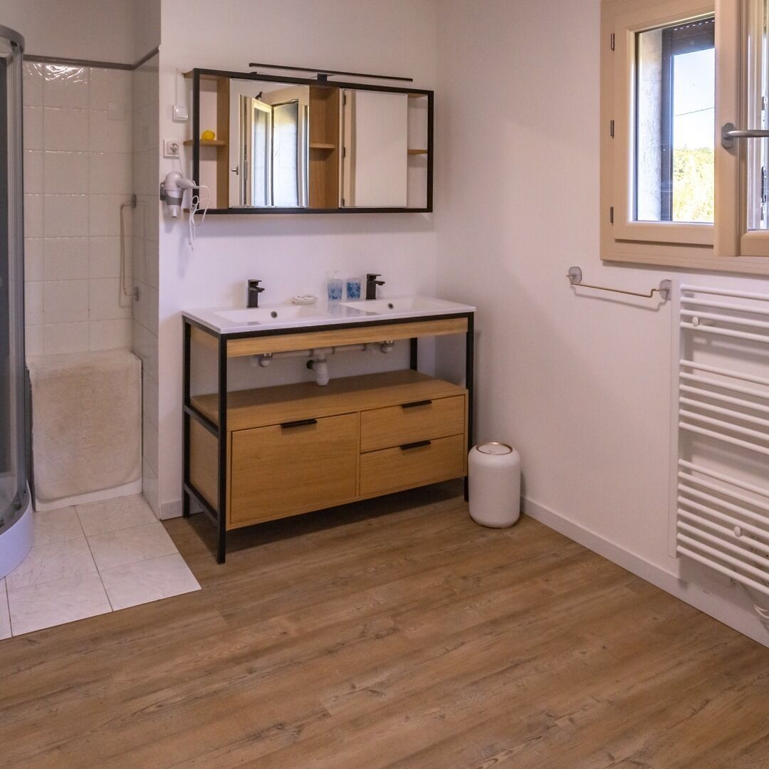 A bathroom with a wooden vanity, a mirror, a shower, and a radiator.