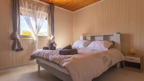 Un dormitorio con cama, mesita de noche, ventana con cortinas y techo de madera.