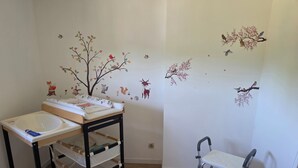 Una habitación con piso de madera, un lavamanos blanco, una mesita con cambiador para bebés, una silla blanca y adhesivos murales de aves y animales.