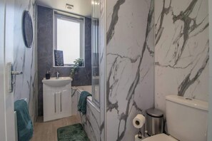 Een badkamer met een marmeren wand, een wastafel, toilet en spiegel.