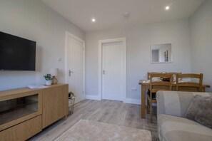 A modern living room with a TV, wooden furniture, a dining area with chairs, and a door.
