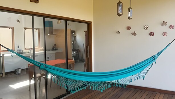 Una hamaca en una habitación con piso de madera, un ventanal corredero que da a una cocina y decoración en las paredes.