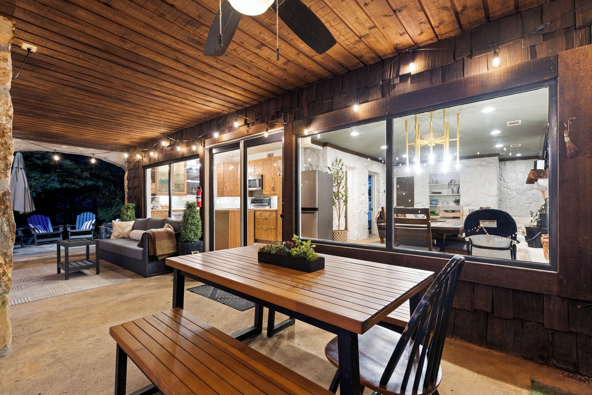 An outdoor patio with wooden furniture, a dining table, and a view into the kitchen area.