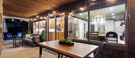 An outdoor patio with wooden furniture, a dining table, and a view into the kitchen area.