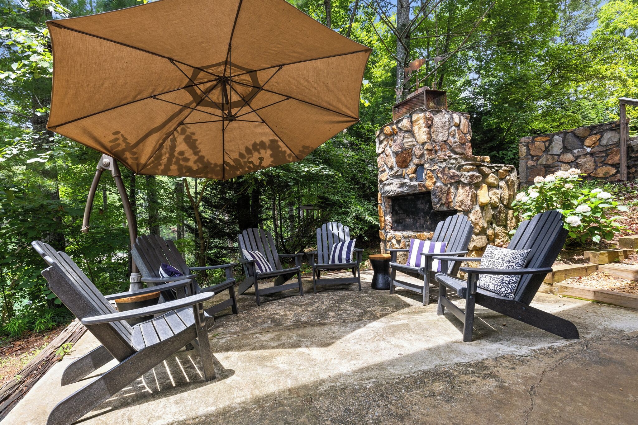 An outdoor seating area with Adirondack chairs, a large umbrella, and a stone fireplace.