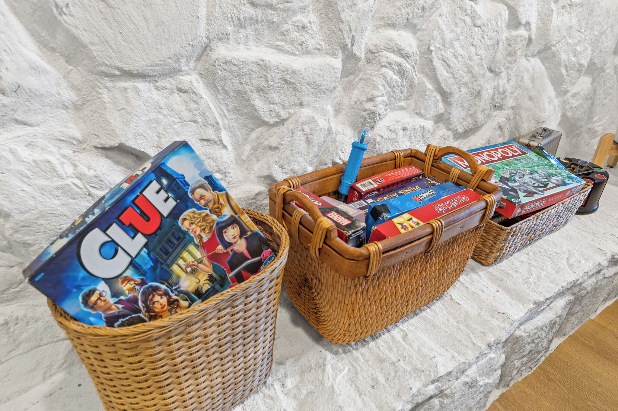 Due cesti di vimini pieni di giochi da tavolo e un giocattolo su un muro bianco con texture.