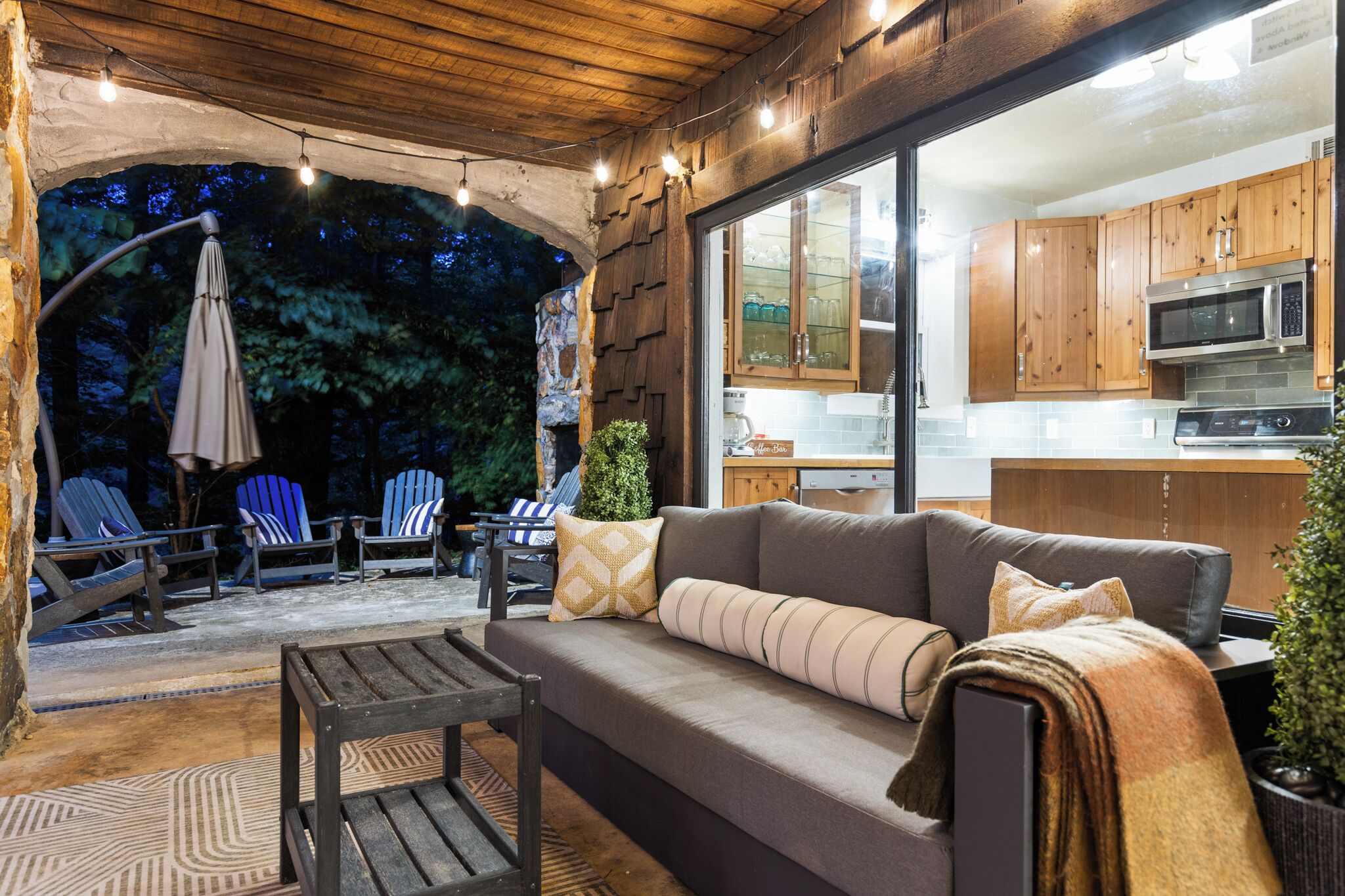 An outdoor patio area with a sofa, chairs, and a table. There is a kitchen visible through a glass door.