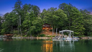Un chalet au bord du lac, doté d’une terrasse et d’un quai abrité, entouré d’une forêt dense.