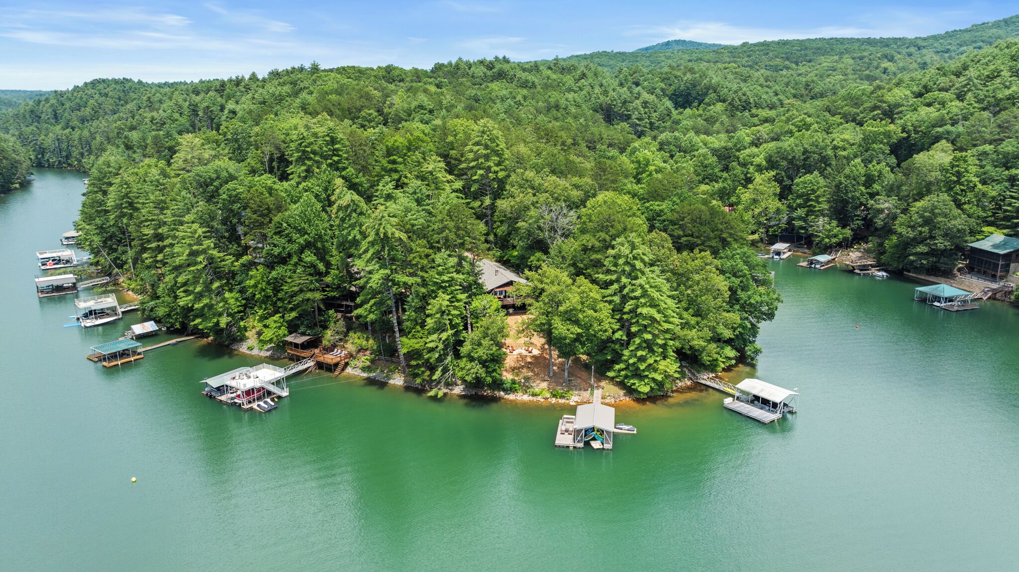 An island with a house surrounded by dense forest, connected to the mainland by a dock.