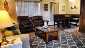 A living room with a sofa, a coffee table, a lamp, and a dining area with a table and chairs.
