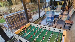 A foosball table in a well-lit room with a view of a garden through large windows. - VELO APPARTEMENT BABY FOOT 3 VRAIES CHAMBRES 1 MINUTES DE LA MER JARDIN VERANDA (Nice)