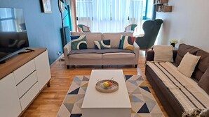A living room with a sofa, a coffee table, and a television on a wooden cabinet. - VELO APPARTEMENT BABY FOOT 3 VRAIES CHAMBRES 1 MINUTES DE LA MER JARDIN VERANDA (Nice)