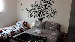 A bedroom with two single beds, each with patterned bedding and pillows, a wall mural of a tree, and a bedside table with a lamp. - IN Club Hostel (Zagreb)