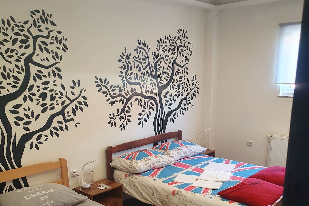 Ein Schlafzimmer mit zwei Einzelbetten, einer Baum-Wandmalerei und einer Heizung.