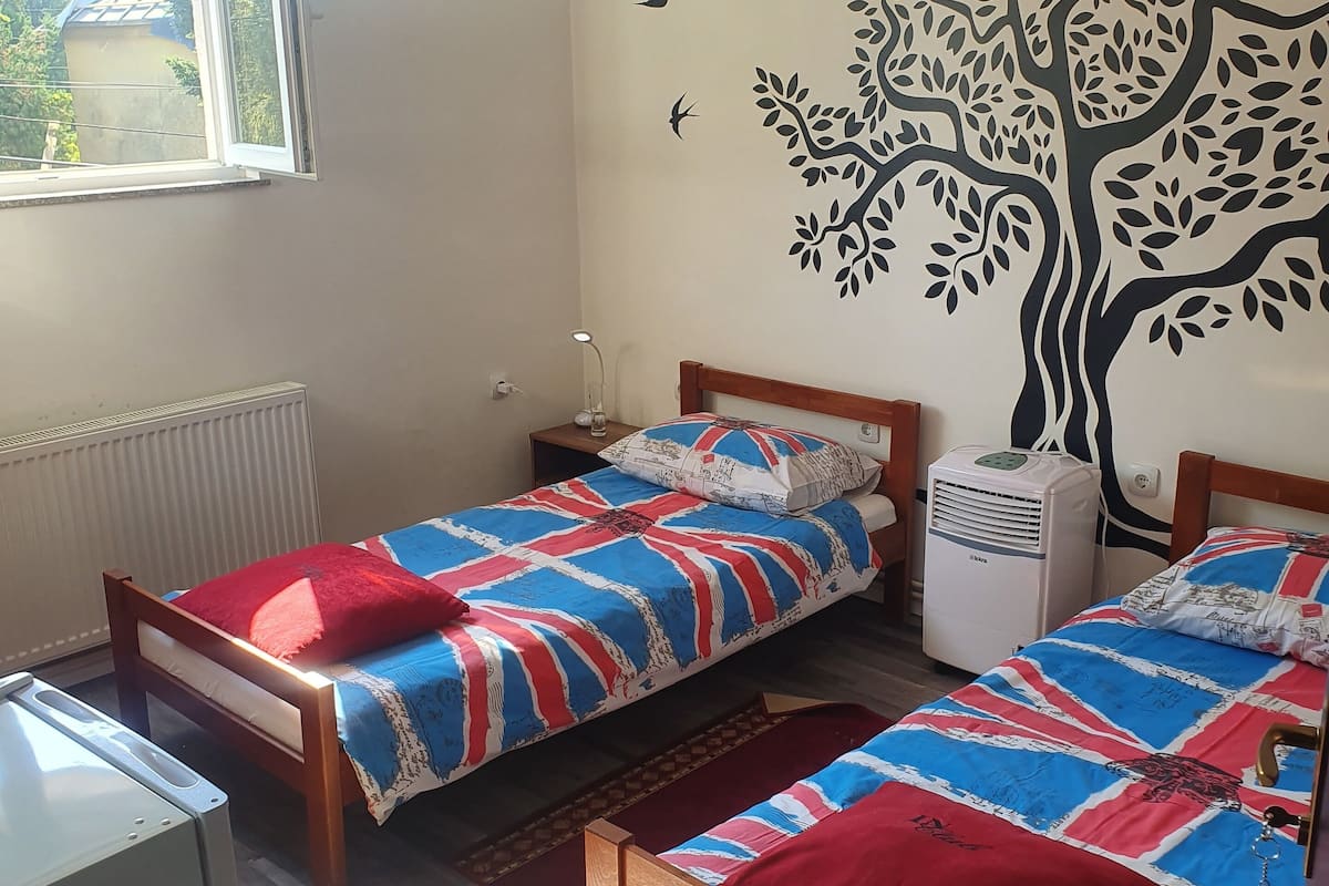 Ein Schlafzimmer mit zwei Einzelbetten, einem Heizkörper, einem Fenster und einem Wandbild.