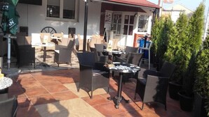 An outdoor patio with multiple tables and chairs, surrounded by potted plants and a building in the background. - IN Club Hostel (Zagreb)