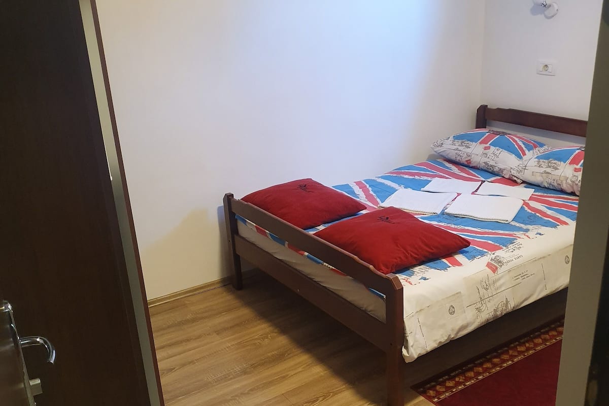 Ein Schlafzimmer mit einem hölzernen Bett, einer roten und weißen Bettdecke und einem roten Zierkissen.