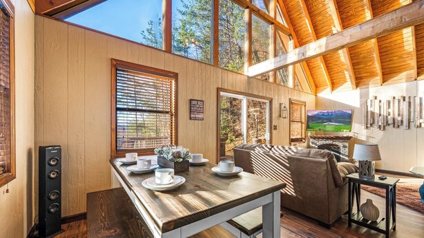 A spacious living area with a wooden dining table, a sofa, and a television. - Summer Getaway with Mountain View from the deck! Close to Dollywood! (Sevierville)