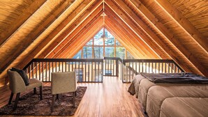 A cozy attic bedroom with wooden beams, a large window, a bed, two chairs, and a small table. - Summer Getaway with Mountain View from the deck! Close to Dollywood! (Sevierville)
