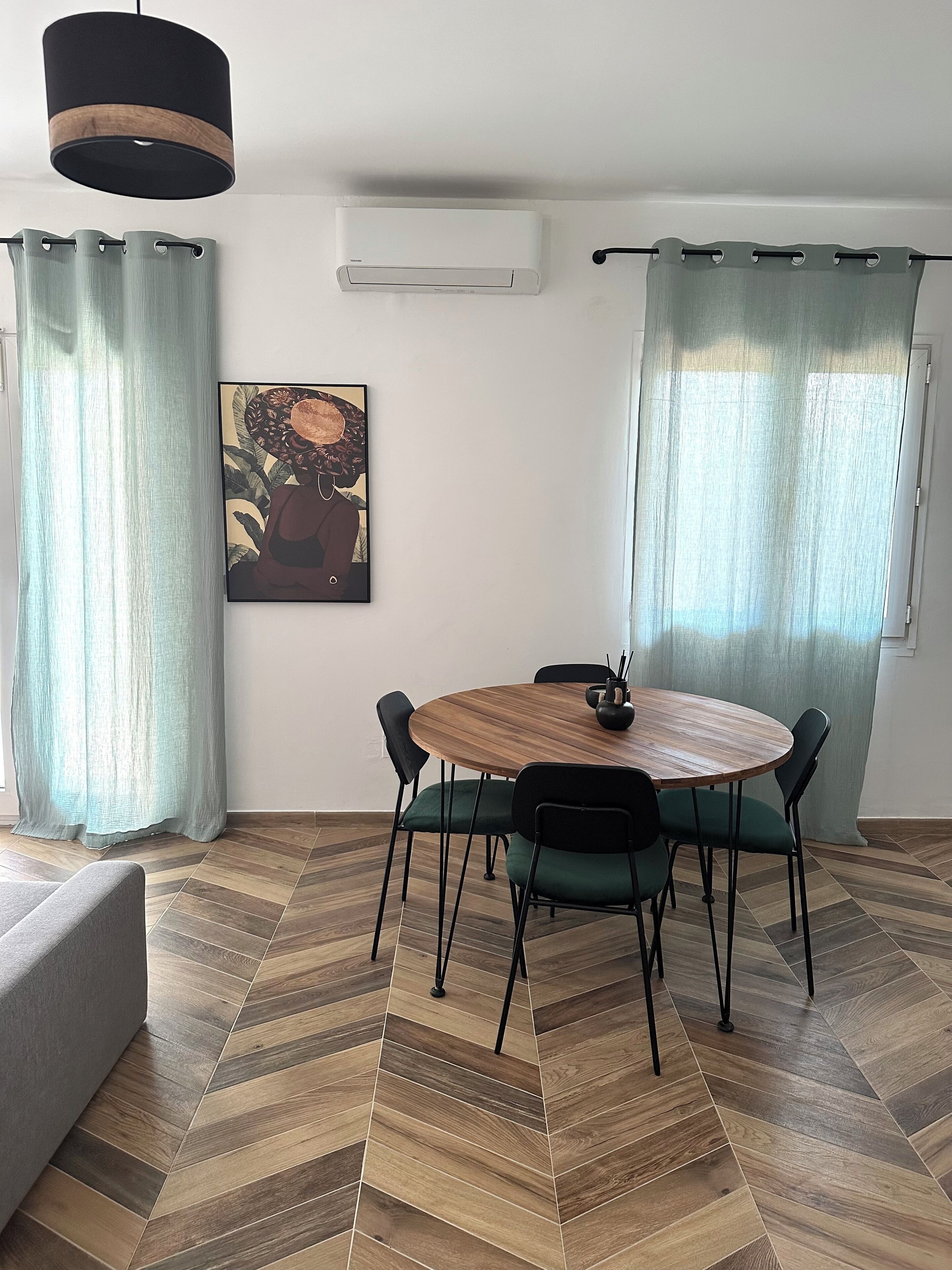 A dining area with a round wooden table, black chairs, and a painting on the wall.