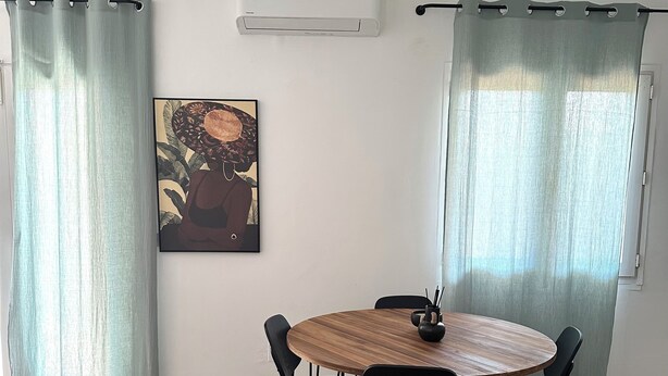 Un comedor con una mesa redonda de madera, sillas negras y un cuadro en la pared.