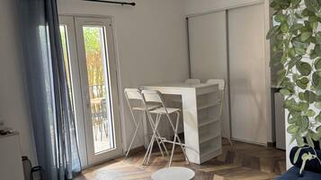 Een moderne woonkamer met een blauwe bank, een witte bijzettafel, een plafondlamp en uitzicht op een balkon met tuinmeubilair.