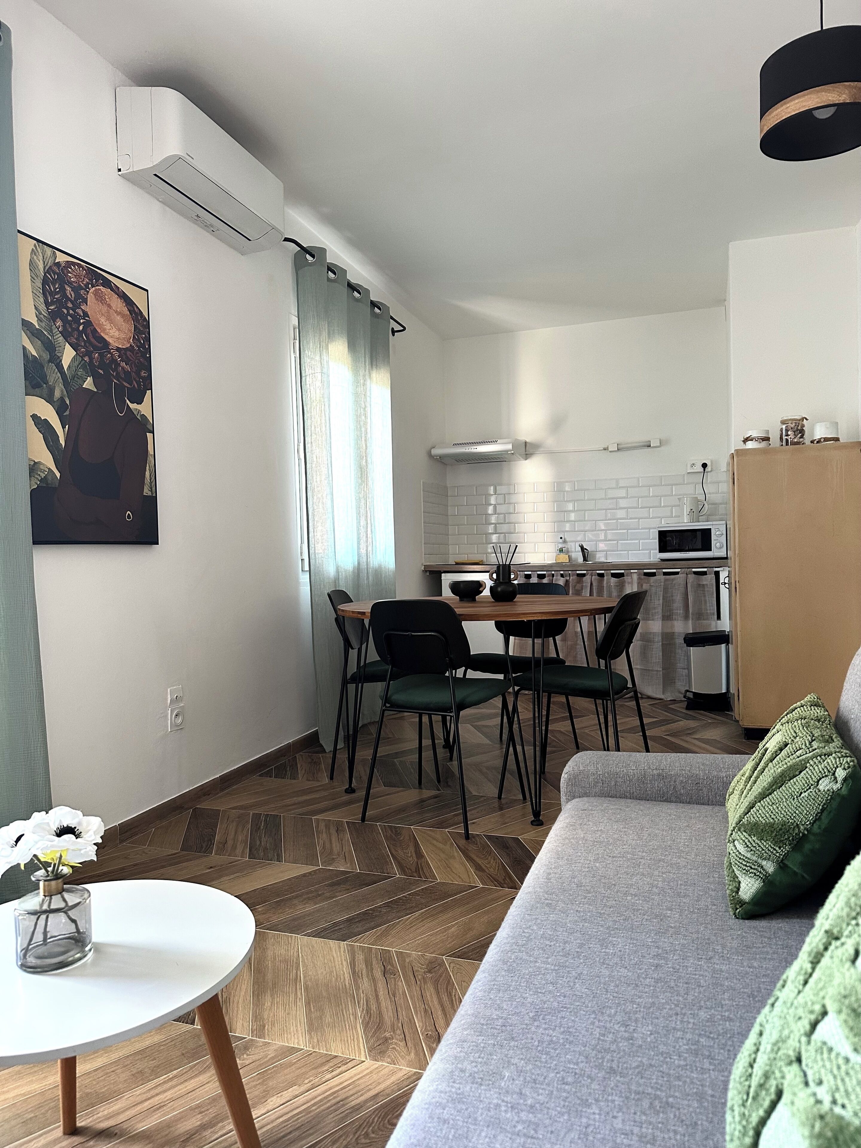 Un salon moderne comprenant un canapé, une table à manger avec des chaises, un coin cuisine avec un four à micro-ondes et un appareil de climatisation.
