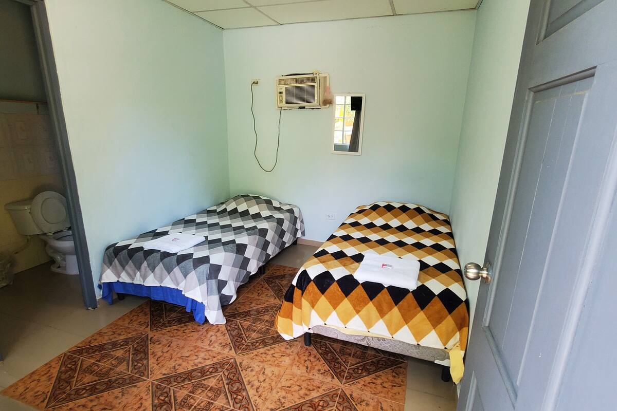 Una habitación con dos camas, ventilador de techo, aire acondicionado y piso con diseño.