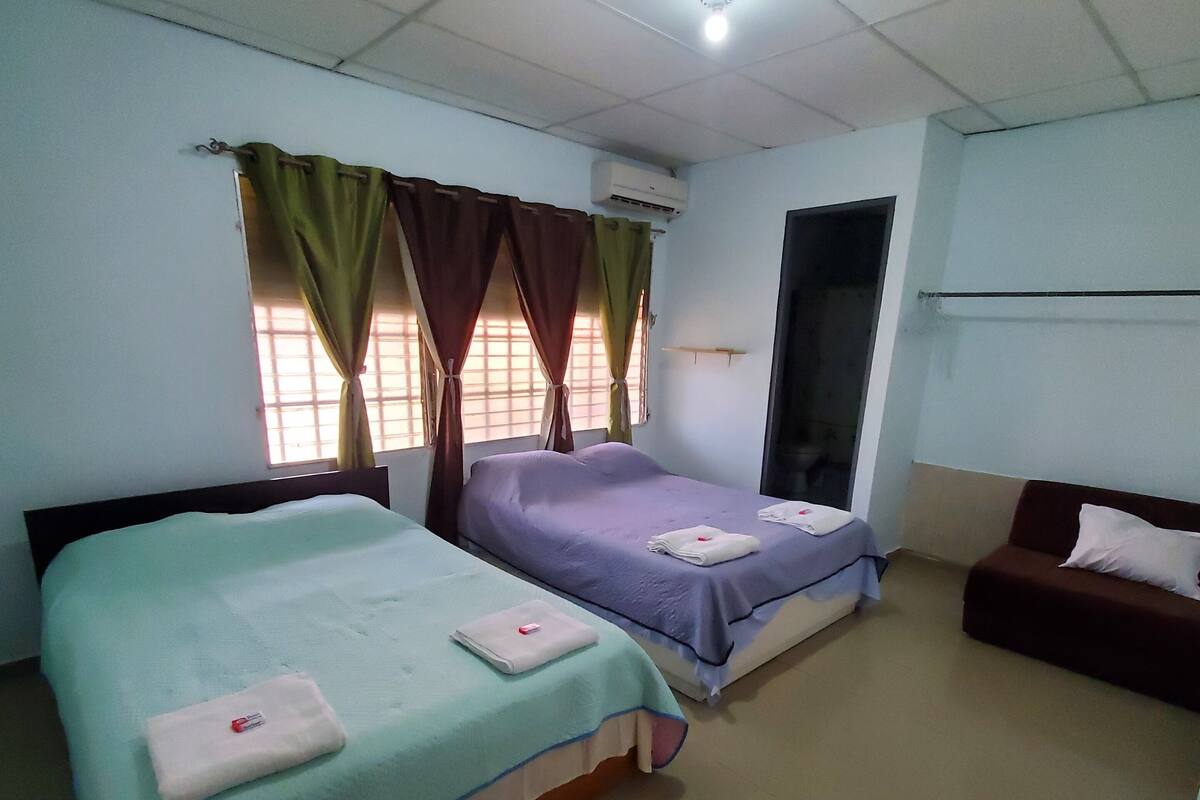 Habitación de hotel con dos camas, un sofá, una ventana con cortinas y un equipo de aire acondicionado.