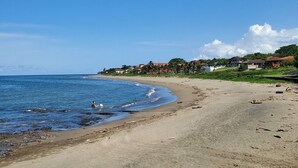 Una playa con cielo azul despejado, orilla arenosa y casas al fondo.