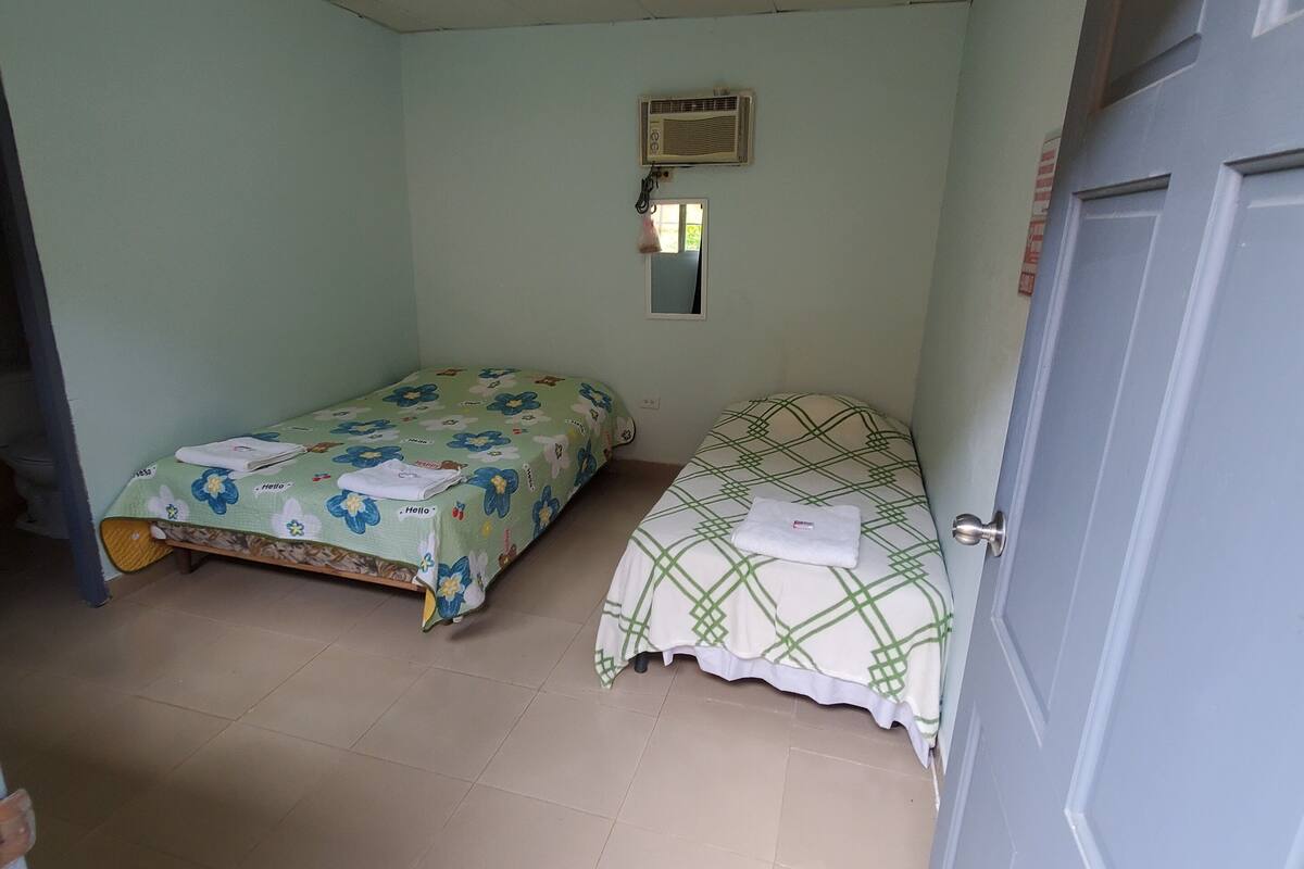 Una habitación con dos camas, ventilador de techo, aire acondicionado y una puerta.