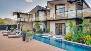 A modern two-story house with a swimming pool, outdoor seating, and lush landscaping.