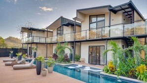 Una casa moderna de dos pisos con piscina, mobiliario exterior y jardines exuberantes.