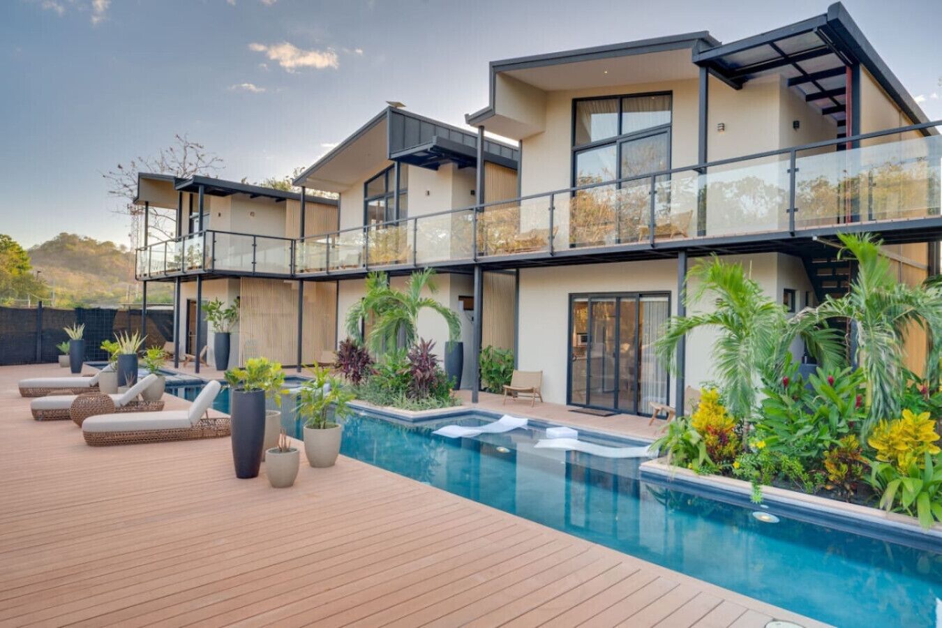 Una casa moderna de dos pisos con piscina, mobiliario exterior y un balcón.