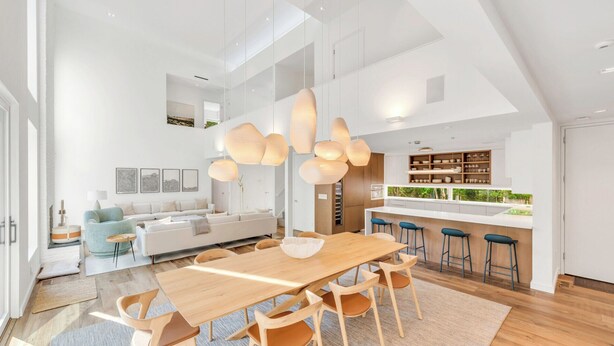 Un'ampia zona giorno con tavolo e sedie in legno, un divano blu chiaro e una cucina con angolo bar.