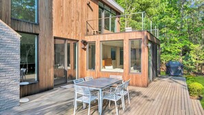 Una casa moderna con una terrazza, un'area pranzo con sedie bianche e un barbecue.