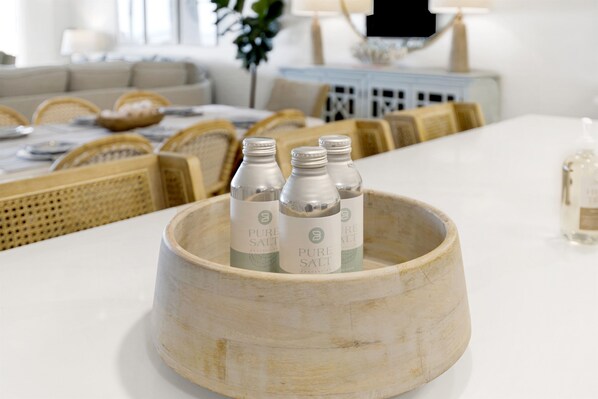 Un plateau en bois contenant trois bouteilles étiquetées « SEL PUR », posé sur une table blanche dans un salon moderne.