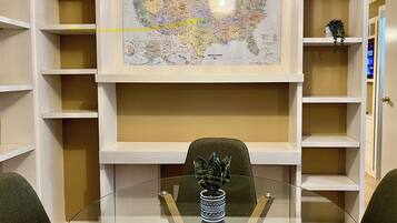 Een kamer met een glazen tafel, een kaart van de Verenigde Staten aan de muur en planken met diverse spullen.