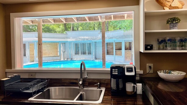 Une cuisine dotée d’une grande fenêtre donnant sur une piscine située dans le jardin.