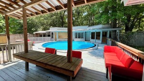 Une terrasse en bois avec une piscine, des meubles d’extérieur rouges et un espace abrité doté d’un toit en métal.