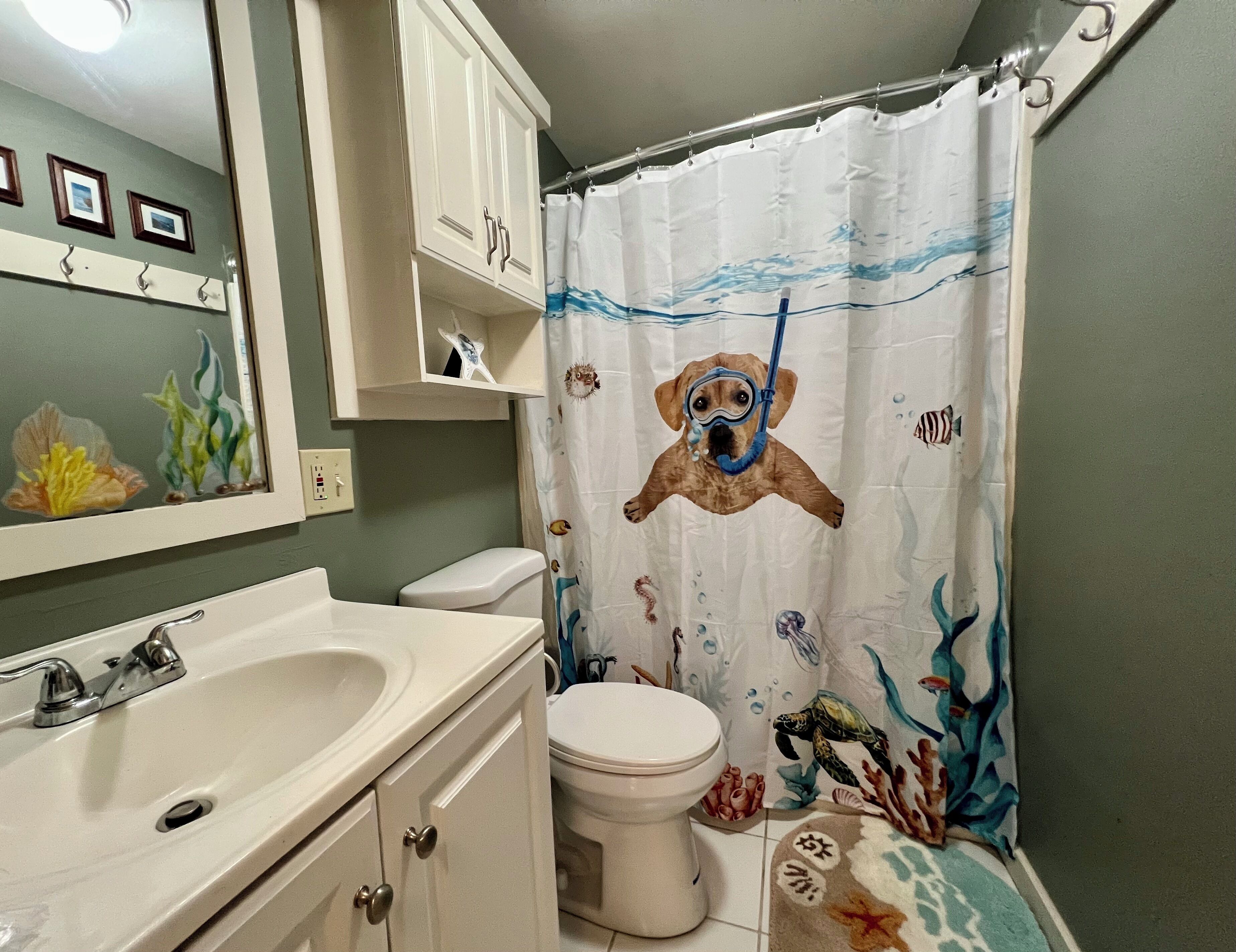 Een badkamer met een wit wastafel, toilet en kastje. Er is een douchegordijn met een zeeschildpad ontwerp.