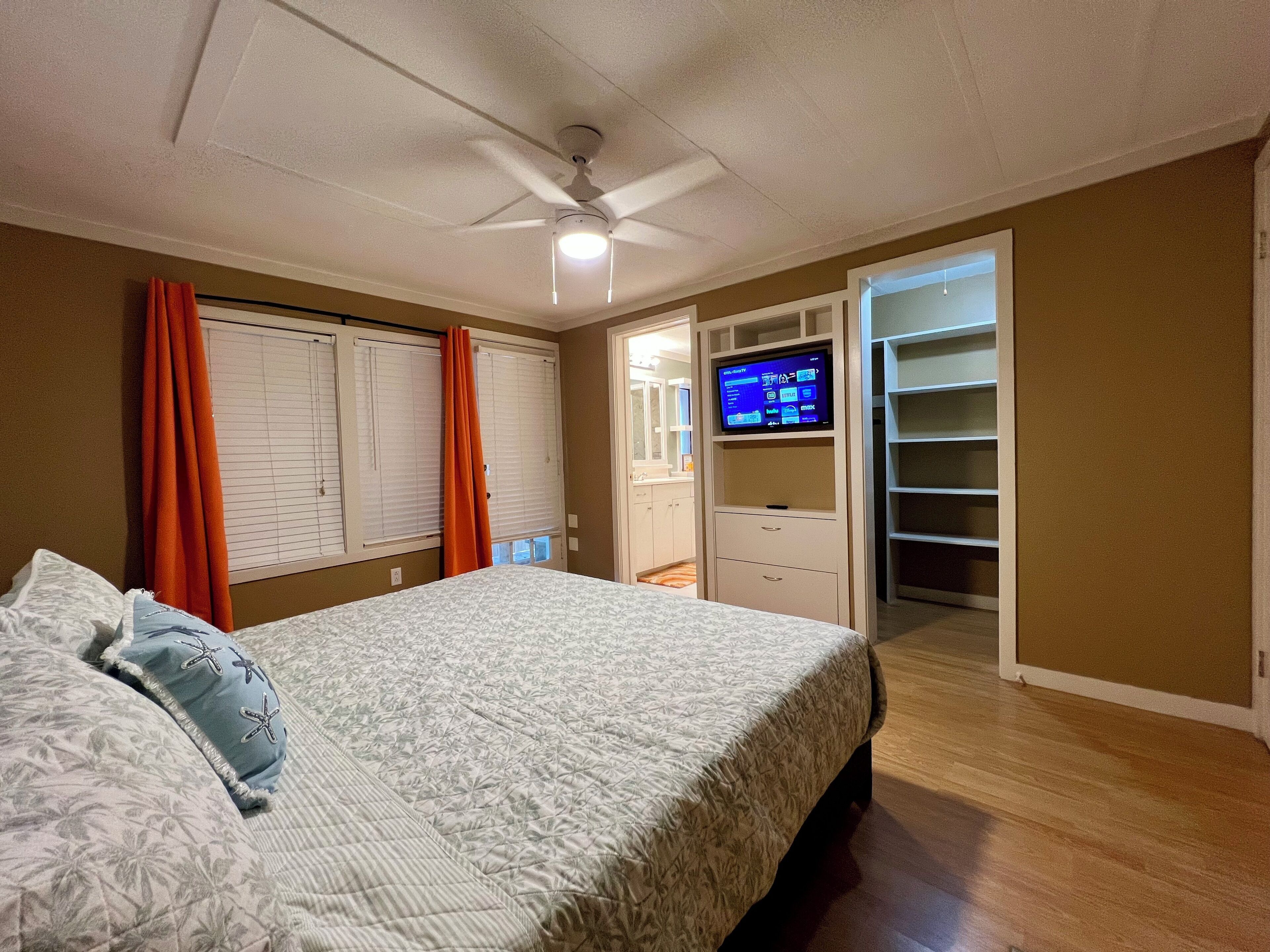 A bedroom with a bed, a ceiling fan, a TV, and a walk-in closet.