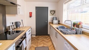 A compact kitchen with a microwave, kettle, and toaster on the countertop, a small sink, and a window with blinds.