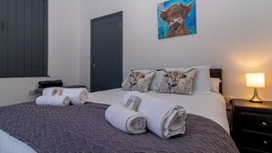A neatly made bed with rolled towels, a painting of a bull, and a bedside lamp.